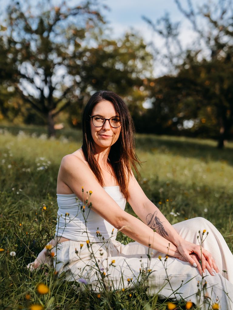 Nelia sitzt mit Brille in einer Blumenwiese und lächelt in die Kamera.